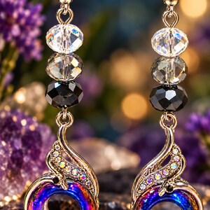 May include: A pair of dangle earrings featuring gold-tone hooks, clear faceted crystal beads, and black faceted beads. The base of each earring is a circular, iridescent purple and blue metal charm accented with small, shimmering clear crystals.