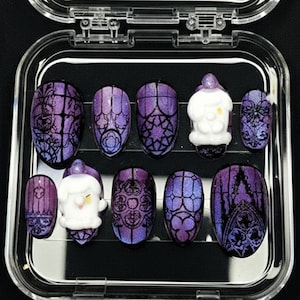 May include: A set of press-on nails in a clear plastic case. The nails feature a purple and black gothic design with a Santa Claus accent nail. The nails are oval-shaped and have a glossy finish.
