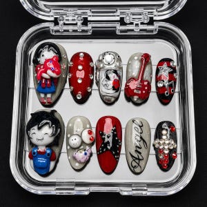 May include: A set of ten press-on nails in a clear plastic case, featuring red, black, and grey designs. Embellishments include 3D cartoon figures, a red guitar, a black star, the word Angel in script, rhinestones, and skull-shaped accents.