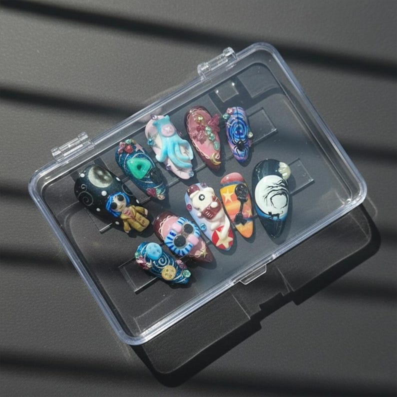 May include: A clear plastic case holding a collection of elaborately decorated artificial nails. The nails feature various designs, including cartoon characters, floral patterns, and abstract art, in a range of colors like blue, pink, and orange.