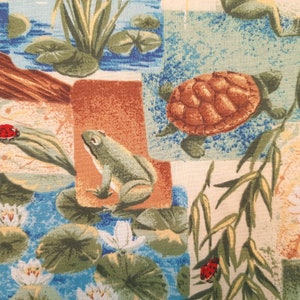 May include: A colorful fabric with a patchwork design featuring a green frog, a brown turtle, lily pads, and red ladybugs. The fabric has a light blue background with a white and green pattern.