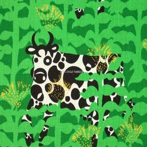 May include: A black and white cow with large, round spots stands in a field of green plants with yellow flowers. The cow is partially obscured by the plants. The text "SPIN CYCLE FABRICS" is visible on the cow's side.