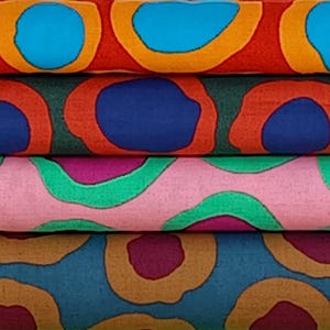 以下が含まれることがあります： 大きな円の繰り返し模様が特徴的な、カラフルな生地のロールのスタック。円は青、オレンジ、緑、ピンク、茶色など様々な色を使用しています。生地は綿または同様の素材のようです。