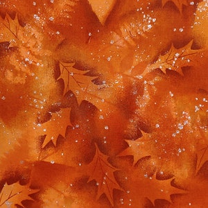 May include: Orange fabric with a pattern of brown leaves and white glitter. The fabric has a soft, textured feel.
