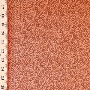 May include: Peach-colored fabric with a repeating pattern of small, dark red floral designs. The fabric is measured with a wooden ruler marked in inches, showing measurements from 17 to 26 inches.