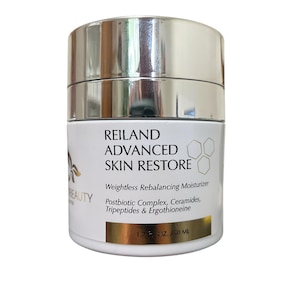 Puede incluir: Un tarro blanco y plateado de crema hidratante Reiland Advanced Skin Restore. La etiqueta incluye el texto "Weightless Rebalancing Moisturizer" y "50 ml". El tarro tiene una tapa plateada y una base blanca con texto negro.