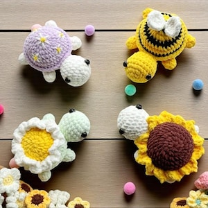 Puede incluir: Juguetes de ganchillo con forma de tortuga, abeja y girasol. La tortuga tiene un caparazón lavanda. La abeja es amarilla y negra. El girasol tiene un centro marrón y pétalos amarillos.