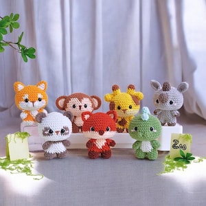 May include: A selection of handmade crochet animal toys, featuring a fox, monkey, giraffe, rhino, panda, red fox, and a dinosaur. Each toy is brightly coloured and has detailed features. A small sign reads "Zoo".