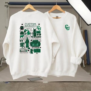 Puede incluir: Se muestran dos sudaderas blancas de manga larga. Una tiene un logotipo "CU" verde en el pecho. La otra presenta un gr&aacute;fico detallado en verde y negro con el texto "Custom University" y "Excellence for CU!"