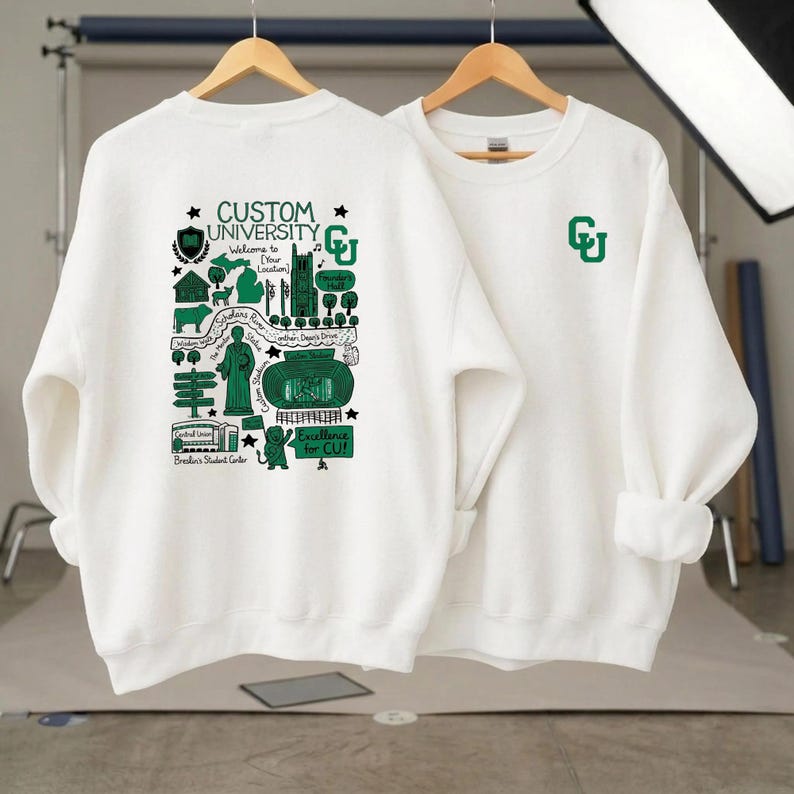 Puede incluir: Se muestran dos sudaderas blancas de manga larga. Una tiene un logotipo "CU" verde en el pecho. La otra presenta un gr&aacute;fico detallado en verde y negro con el texto "Custom University" y "Excellence for CU!"