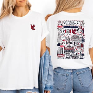 Puede incluir: Camisetas blancas con un dise&ntilde;o rojo y negro. Una camiseta tiene un peque&ntilde;o logotipo en la parte delantera, la otra tiene un dise&ntilde;o detallado en la parte trasera con el texto "UNIVERSITY CUSTOM" y "Home of the CUSTOM CREATORS".