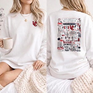 Puede incluir: Sudadera blanca con un peque&ntilde;o logotipo rojo y blanco en la parte delantera y un gr&aacute;fico detallado en la parte trasera. El gr&aacute;fico trasero incluye el texto "UNIVERSITY CUSTOM" y varias ilustraciones en rojo, blanco y negro.