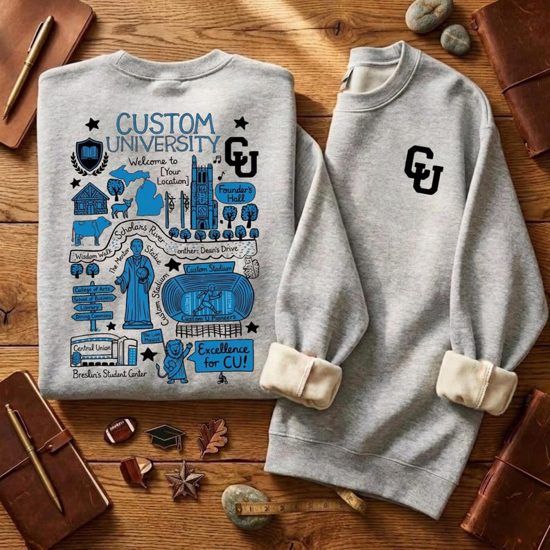 Puede incluir: Dos sudaderas grises con pu&ntilde;os color crema se muestran sobre una superficie de madera. Una sudadera presenta un gr&aacute;fico azul con el texto "CUSTOM UNIVERSITY" y varias ilustraciones. La otra tiene un logotipo "CU" negro.
