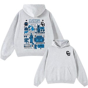 Puede incluir: Sudadera con capucha gris claro con bolsillo delantero y capucha. La parte delantera presenta un gr&aacute;fico azul y blanco con el texto "CUSTOM UNIVERSITY" y "Welcome to [Your Location]" y un logotipo m&aacute;s peque&ntilde;o. La parte trasera tiene un peque&ntilde;o logotipo "CU".