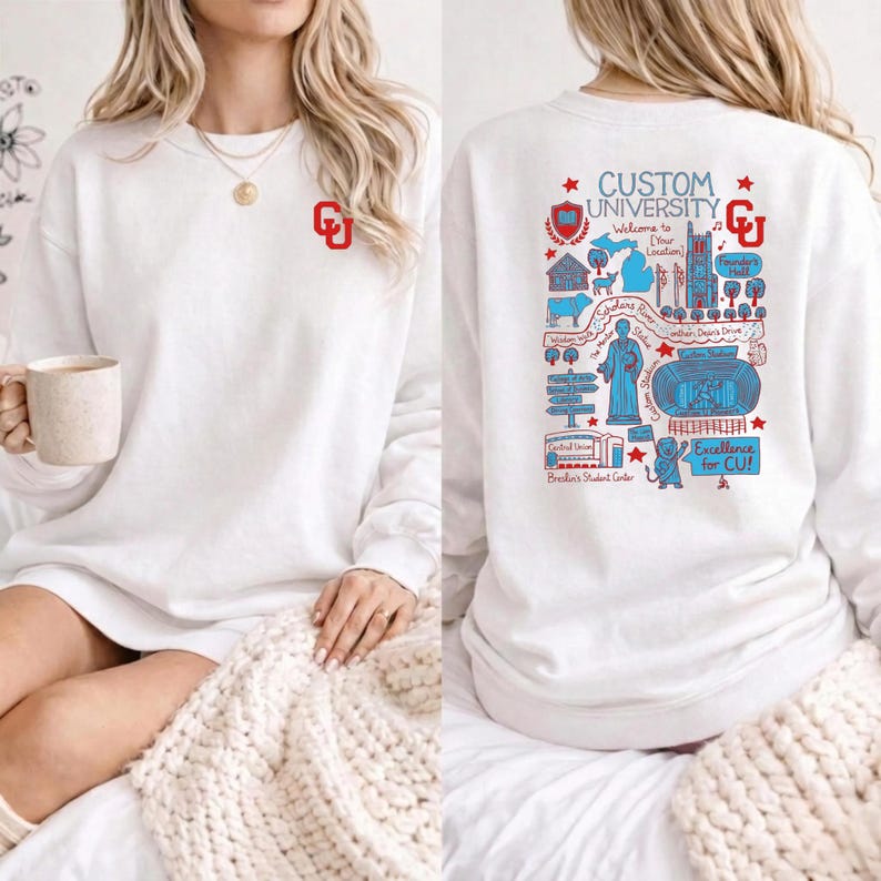 Puede incluir: Sudadera blanca con el logo "CU" rojo. La parte trasera presenta un gr&aacute;fico detallado en rojo y azul con el texto "CUSTOM UNIVERSITY" y "Excellence for CU!" junto con varios puntos de referencia universitarios.
