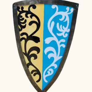 May include: A shield-shaped decorative item with a dark metal frame. The shield is divided vertically into yellow and blue sections, each adorned with a stylized floral design in black and white. The shield has a medieval aesthetic.