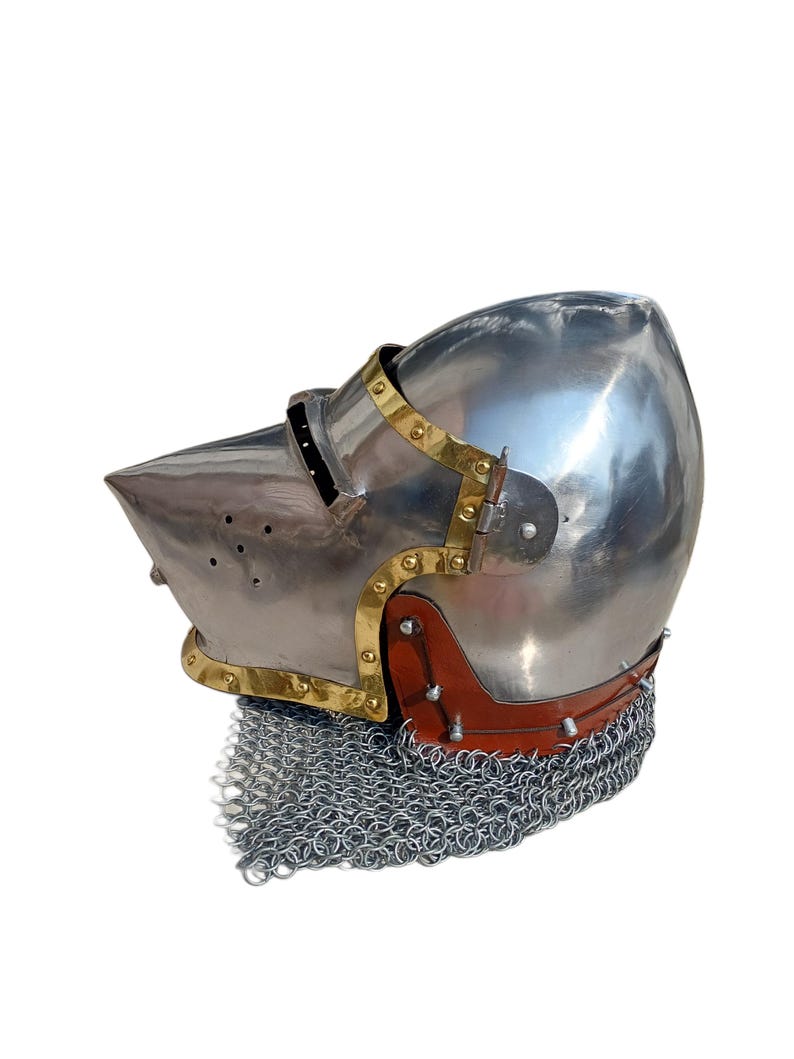May include: A polished steel helmet with a pointed visor and brass detailing. The helmet has a leather neck guard and a chainmail lower edge. This medieval-style helmet is suitable for historical reenactment or display.
