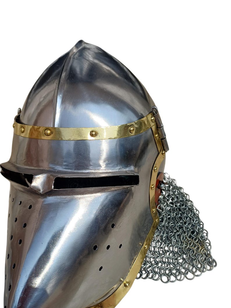 May include: A polished steel medieval helmet with a pointed top, brass trim, and a visor with a narrow eye slit. The helmet features a chainmail aventail and is designed for protection.