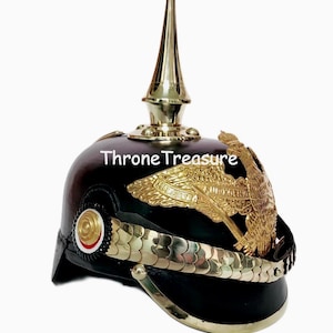 May include: Black Prussian Pickelhaube helmet with a gold-colored spike, eagle emblem, and trim. The helmet has the text "Throne Treasure" on the front. A historical military collectible.