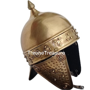 May include: A bronze-colored Roman helmet with a pointed top and decorative trim. The helmet features a curved design with cheek guards and the text "Throne Treasure". The helmet is likely a replica or decorative piece.