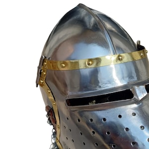 May include: A shiny, silver-coloured medieval helmet with a brass band around the brow, secured with rivets. The helmet has a visor with eye slits and small ventilation holes. A chainmail neck guard is present.