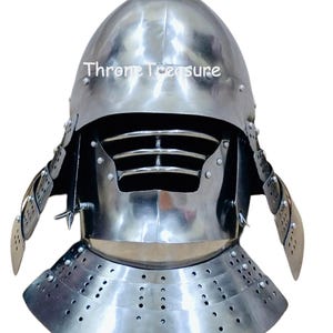 Pode incluir: Um capacete de aço polido com uma parte superior pontiaguda e construção rebitada. O capacete apresenta uma proteção facial com fendas horizontais e placas laterais articuladas. O texto "Throne Treasure" é visível.