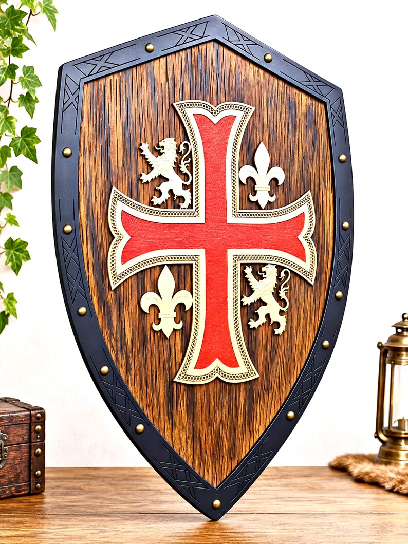 May include: A wooden shield featuring a large red cross at the center, flanked by two white lions and two white fleur-de-lis symbols. The shield has a dark, textured wood grain finish and a black border accented with small brass-colored studs.