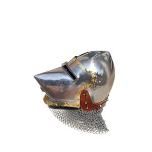 May include: A polished metal helmet with a pointed visor, brass detailing, and a leather and chainmail neck guard. The helmet is designed for protection and historical reenactment.