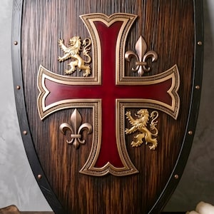 May include: A decorative wooden shield featuring a dark brown wood grain finish and a black metal border with rivets. A large red cross is centered on the shield, flanked by two gold-colored rampant lions and two silver-toned fleur-de-lis emblems.