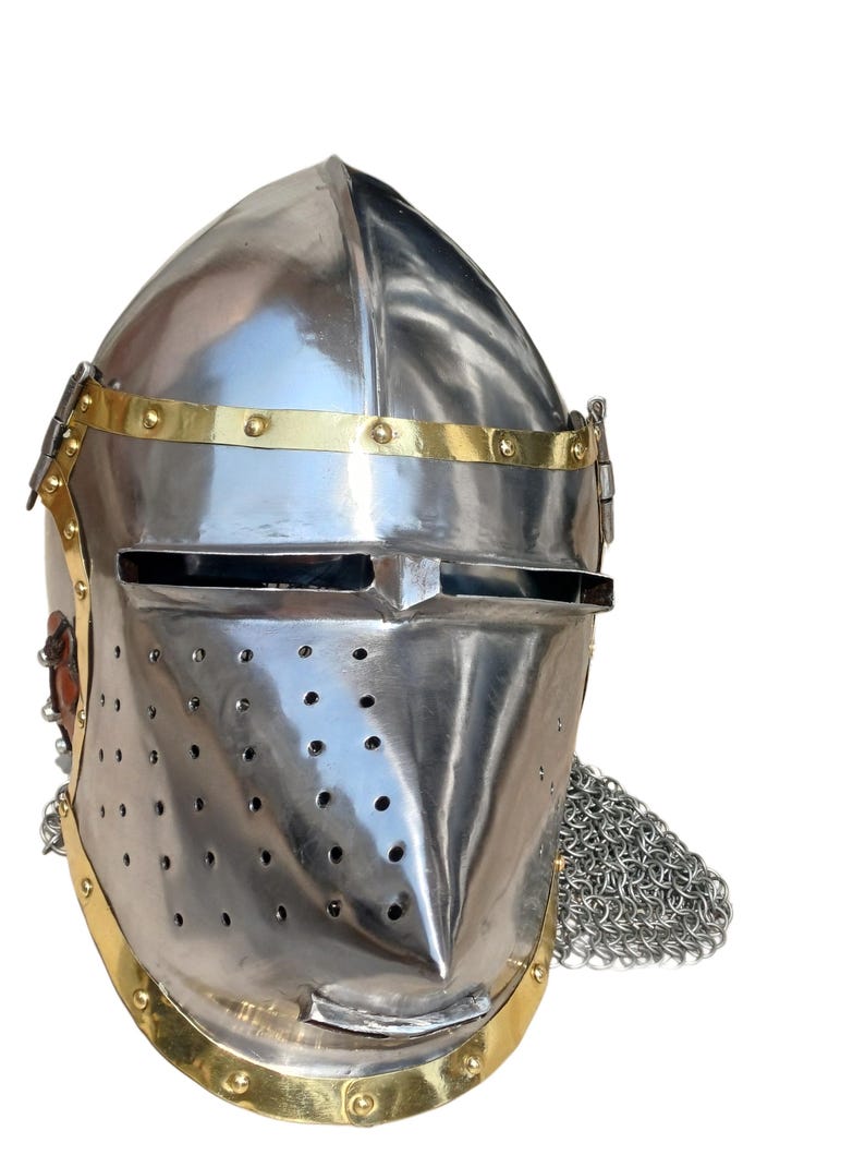 May include: A polished steel knight's helmet with brass detailing. The helmet has a pointed visor, ventilation holes, and a chainmail neck guard. The design is reminiscent of medieval armour.
