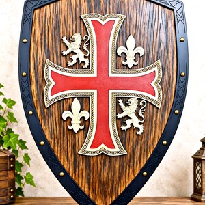 May include: A wooden shield featuring a central red cross with gold trim, flanked by two white lions and two white fleur-de-lis symbols. The shield has a dark wood grain finish and a black border accented with evenly spaced gold-colored metal studs.