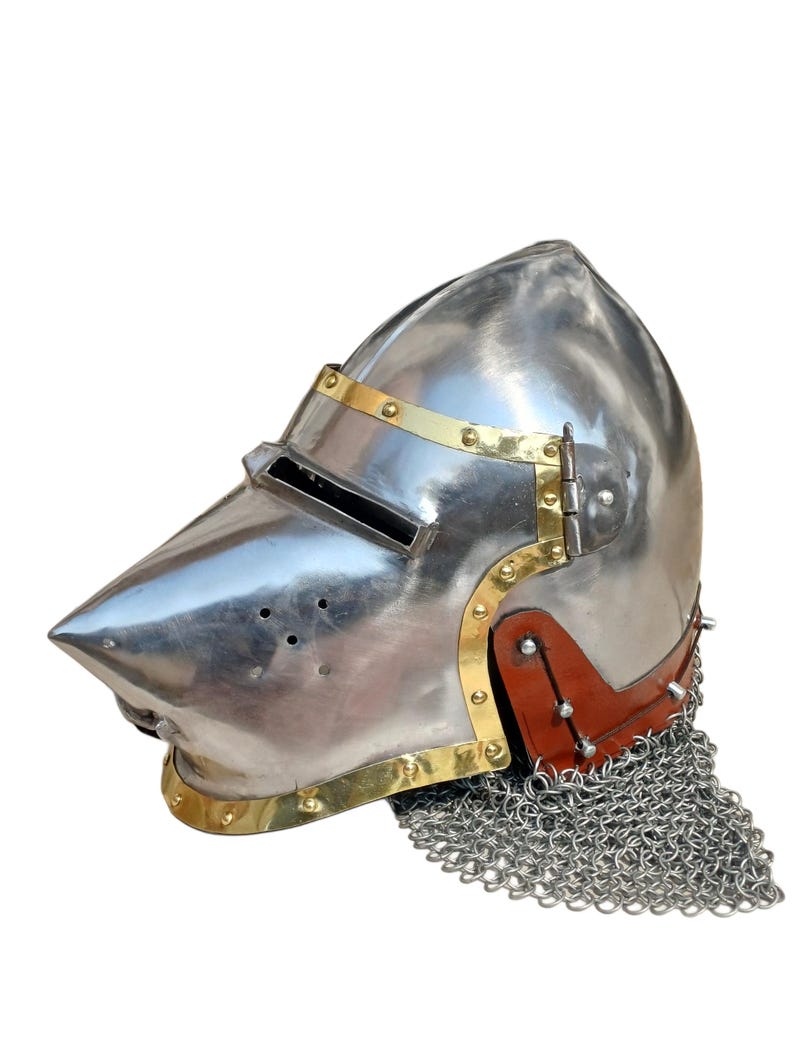 May include: A polished steel helmet with a pointed visor and brass detailing. The helmet has a riveted leather neck guard and a chainmail aventail. This medieval-style helmet is suitable for historical reenactment or display.