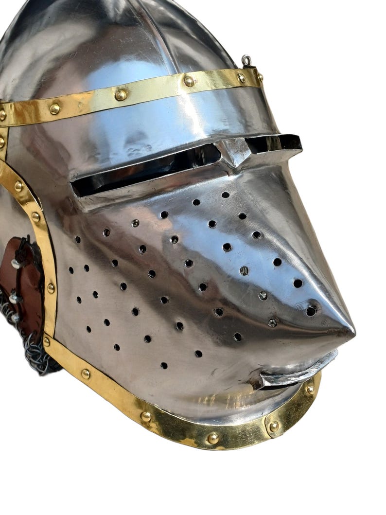 May include: A polished steel helmet with brass detailing. The helmet has a pointed visor with ventilation holes and a curved lower edge. Brass bands with rivets adorn the base and top. This helmet is likely for historical reenactment or display, reflecting medieval armour.