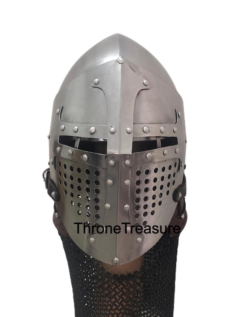 Pu&ograve; includere: Un elmo medievale in metallo color argento con una piastra frontale a forma di croce, fessure orizzontali per gli occhi e una sezione inferiore perforata per la ventilazione. L'elmo presenta rivetti visibili e una maglia di ferro nera.