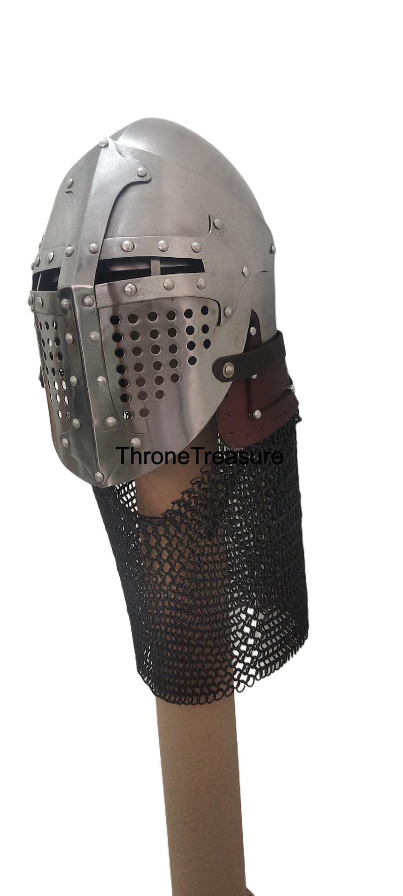 Pu&ograve; includere: Un elmo in stile medievale in metallo color argento con una piastra frontale rivettata dotata di una fessura orizzontale per gli occhi e una visiera perforata. L'elmo include un cinturino in pelle marrone scuro e un camaglio in maglia di ferro nero. Il testo ThroneTreasure &egrave; visibile.