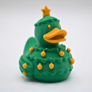 May include: A green duck figurine with an orange beak and star-shaped crown. The duck is decorated with orange ornaments and has a ruffled collar. This festive decoration is perfect for the holiday season.