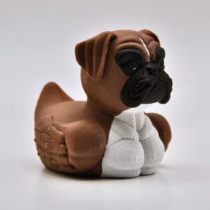 May include: A brown and white Boxer dog figurine. The dog has a brown body, head, and ears, with a black muzzle and white paws. The figurine is a decorative item, likely a collectible or a toy.