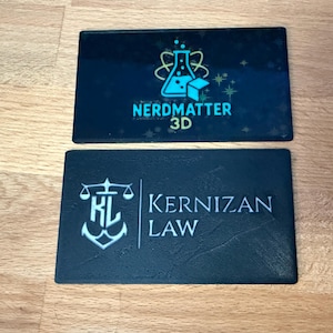 May include: Two rectangular business card holders. One is dark blue with the text "NERDMATTER 3D" and a science-themed logo. The other is black with the text "KERNIZAN LAW" and a scale logo.
