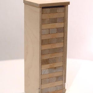 Könnte beinhalten: Ein hölzernes Jenga-Spielset in einer rechteckigen Holzkiste. Die Spielsteine sind in der Kiste gestapelt und spielbereit. Die Kiste ist aus hellem Holz gefertigt und hat ein schlichtes, klares Design.