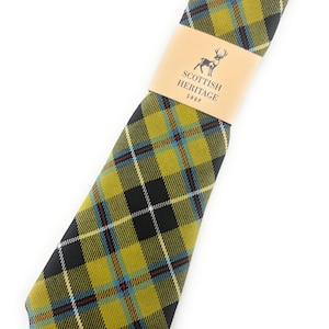 May include: A tartan tie in olive green, black, and blue. A brown paper band with a deer logo and the text "SCOTTISH HERITAGE SHOP" is wrapped around the tie. The tie is displayed at an angle.