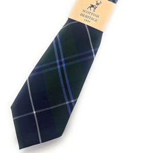 Peut inclure: Une cravate à carreaux bleu marine et vert avec des accents bleus et blancs. La cravate est enveloppée d'une bande de papier beige avec l'inscription "Scottish Heritage Shop" et un logo de cerf. Un accessoire classique.
