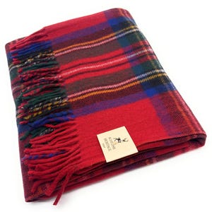 Può includere: Una coperta di tartan rosso piegata con un bordo a frange. La coperta presenta un classico motivo a quadri in rosso, verde, blu e giallo. È attaccata una piccola etichetta con la scritta "Scottish Heritage".