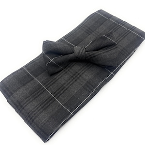 May include: A dark gray plaid bow tie and matching pocket square set. The bow tie is pre-tied and sits atop the folded pocket square. Both pieces feature a classic plaid pattern with thin white lines.