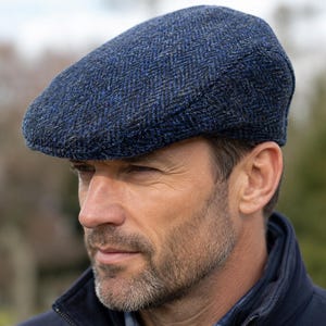 Puede incluir: Una gorra plana con un patrón de espiga texturizado en tonos azul oscuro y negro. La gorra presenta una corona redondeada y una visera corta y rígida en la parte delantera, confeccionada con una tela tejida con un patrón multicolor visible.