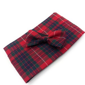 May include: A red, green, and navy plaid bow tie and matching pocket square set. The bow tie is pre-tied and sits atop the folded pocket square. The plaid pattern features a repeating grid of red, green, navy, and white lines.