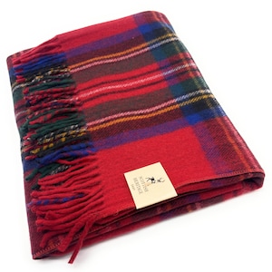 Könnte beinhalten: Eine gefaltete rote Tartandecke mit Fransen. Die Decke hat ein klassisches Karomuster in Rot, Grün, Blau und Gelb. Ein kleines Etikett mit dem Text "Scottish Heritage" ist angebracht.