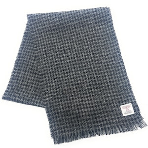 May include: A gray and black houndstooth pattern scarf with fringed edges. The scarf has a woven texture and a small white tag with text. The scarf is made of a soft, warm material.