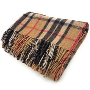 May include: Folded tan plaid blanket with black, red, and white accents. The blanket has a fringed edge in tan, black, and white. The blanket is folded and appears soft and warm.