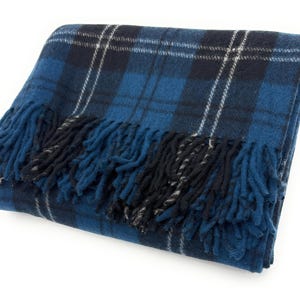 Pode incluir: Cobertor xadrez azul dobrado com franjas. O cobertor apresenta um padrão xadrez clássico em tons de azul, preto e branco. As franjas são azul escuro e preto. O cobertor é dobrado cuidadosamente, mostrando sua textura e design.