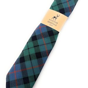 May include: A folded necktie with a green, blue, and black plaid pattern, accented with red lines. The tie is wrapped with a tan paper band that reads "Scottish Heritage Shop" and features a deer logo.